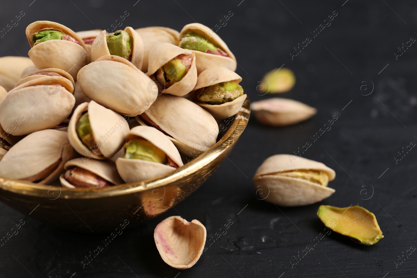 Photo of Tasty pistachios in bowl on black table, closeup. Space for text