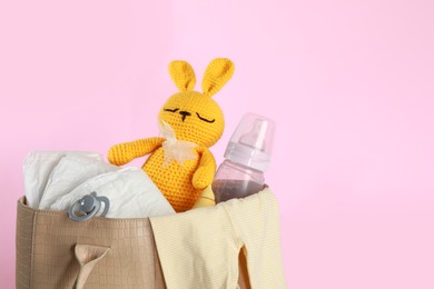 Photo of Mother's bag with baby's stuff on pink background. Space for text