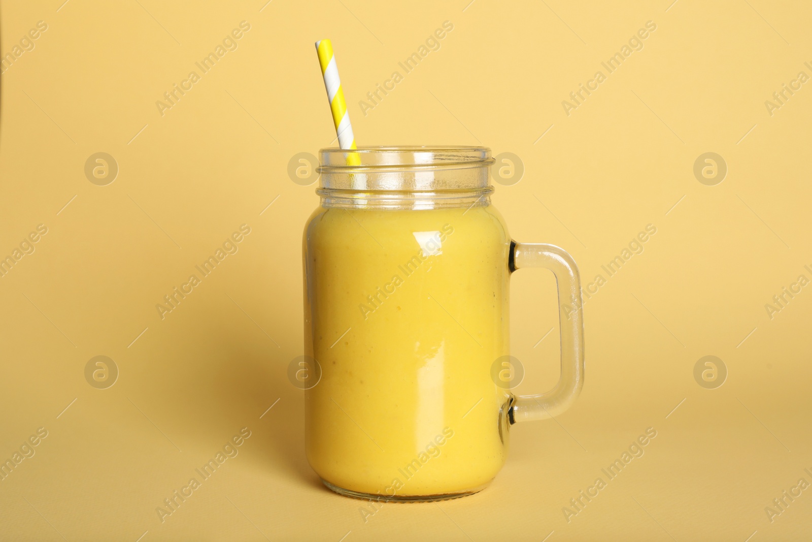 Photo of Mason jar of tasty smoothie with straw on beige background