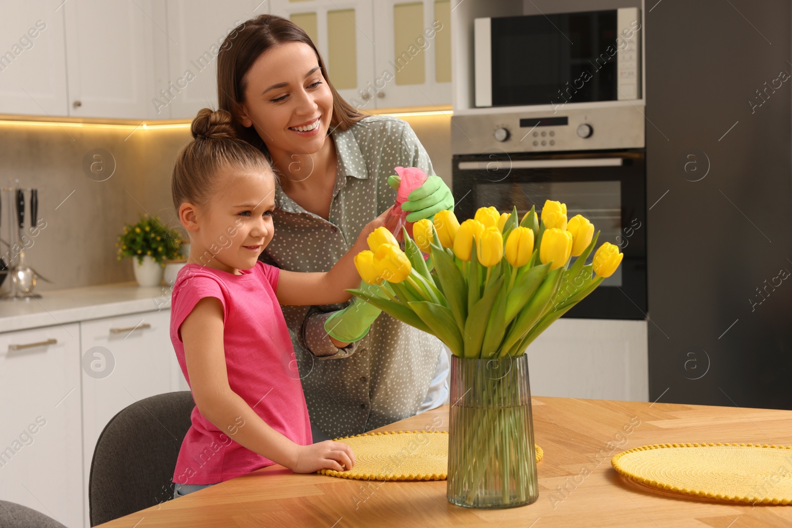 Photo of Spring cleaning. Mother and daughter spraying beautiful bouquet of yellow tulips with water at home