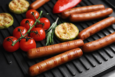 Photo of Cooking delicious fresh sausages with vegetables on modern grill