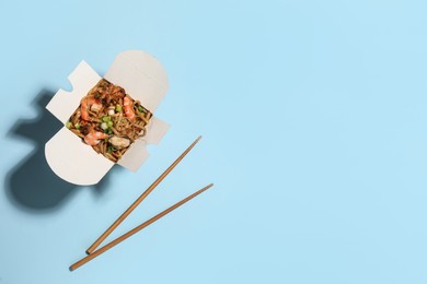 Photo of Noodle wok with chopsticks on light blue background, flat lay. Space for text