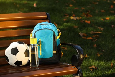 Photo of Backpack, soccer ball and bottle of water on bench in park, space for text