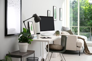 Comfortable workplace with modern computer and houseplants in room. Interior design