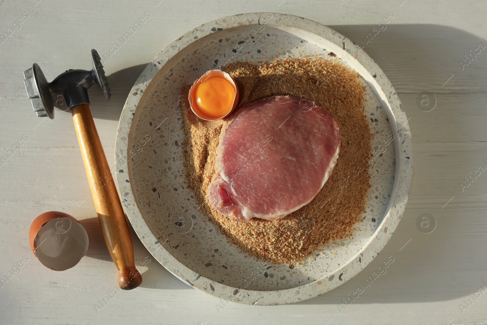 Photo of Cooking schnitzel. Raw pork chop, meat mallet and ingredients on white wooden table, flat lay