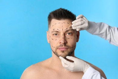 Doctor examining man's face before plastic surgery operation on blue background