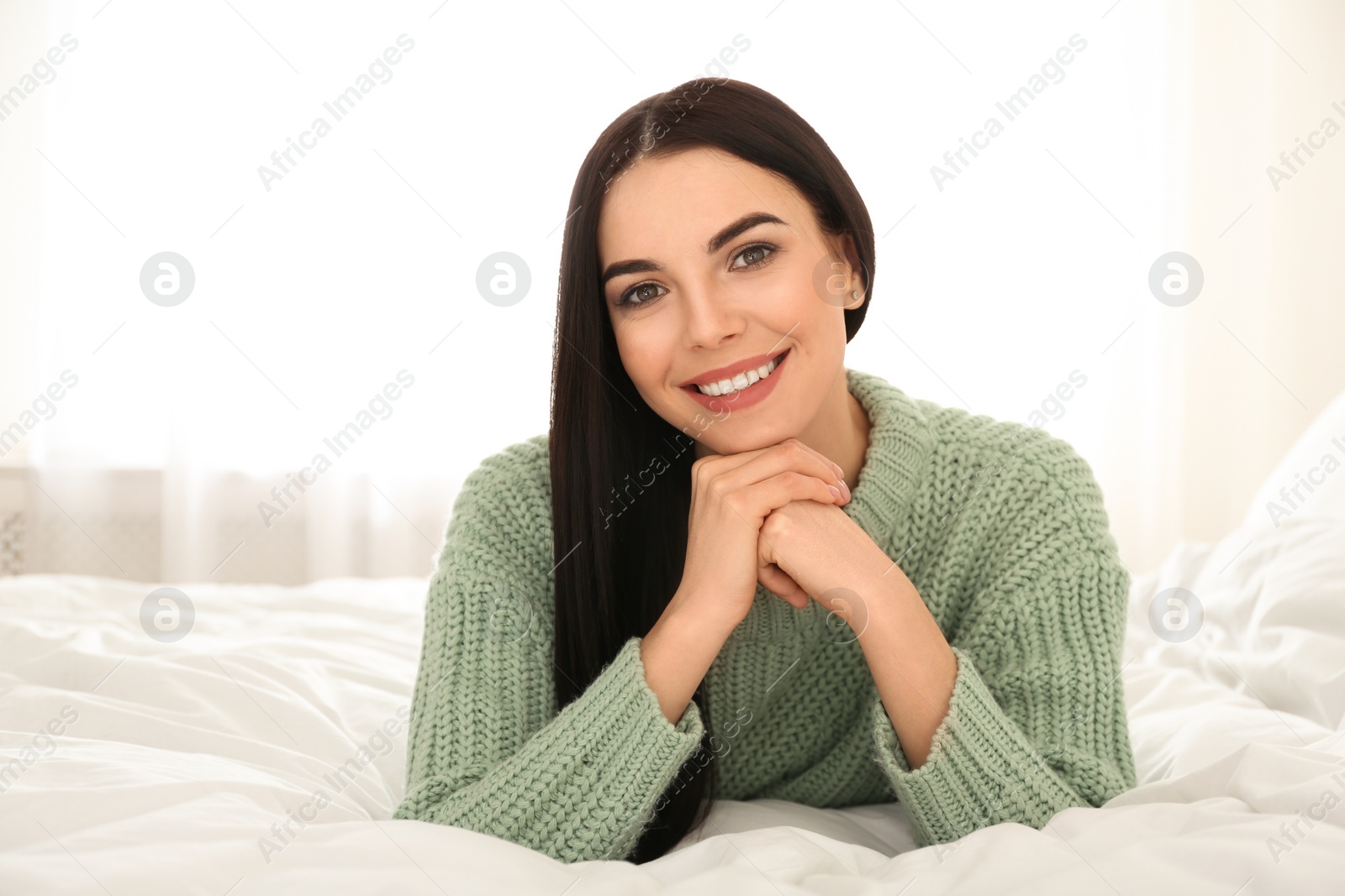 Photo of Young woman wearing warm sweater on bed at home. Winter season