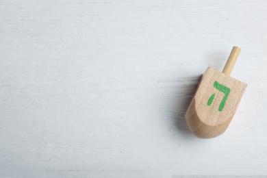 Hanukkah traditional dreidel with letter He on white wooden table, top view. Space for text