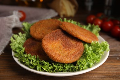 Photo of Delicious fried breaded cutlets with lettuce on wooden table, closeup