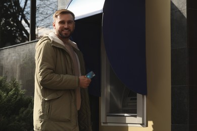 Photo of Happy man with credit card near cash machine outdoors