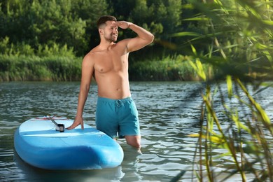 Man standing near SUP board in river water on sunny day