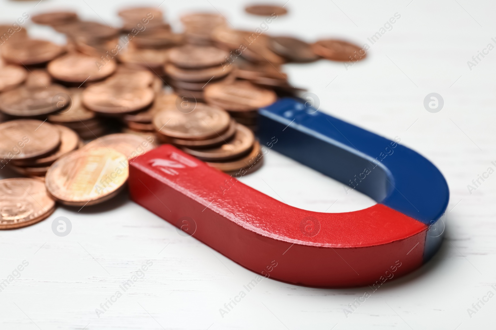 Photo of Magnet attracting coins on wooden background, closeup. Business concept