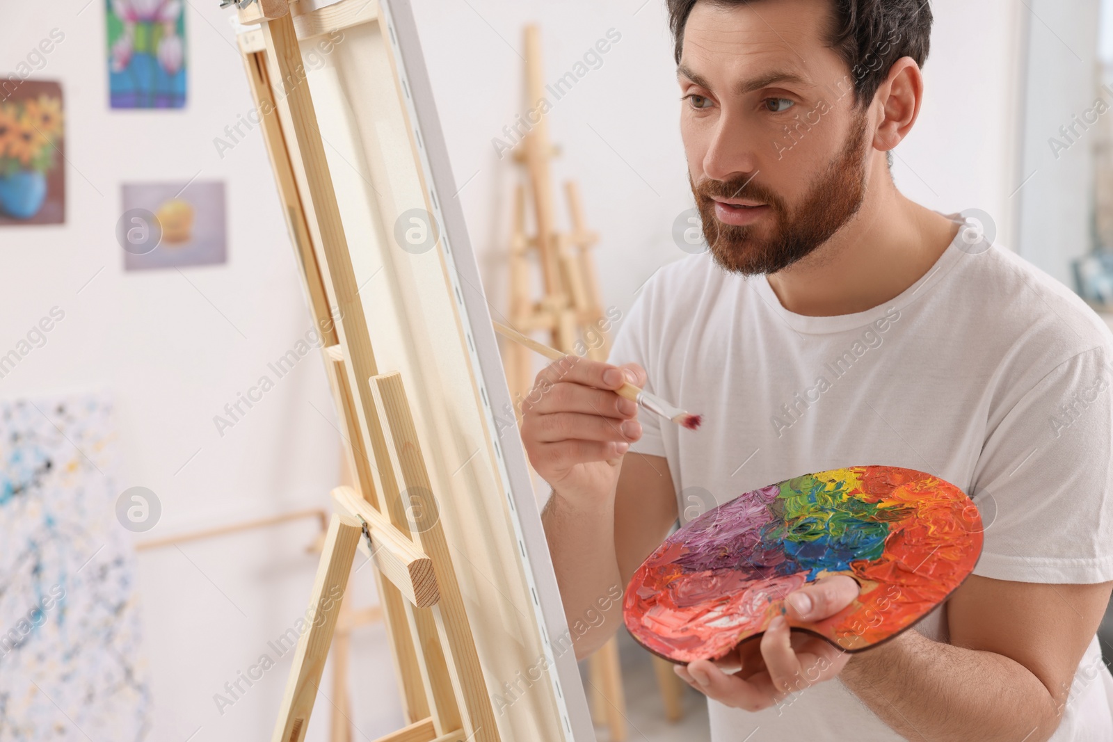 Photo of Man painting in studio. Using easel to hold canvas