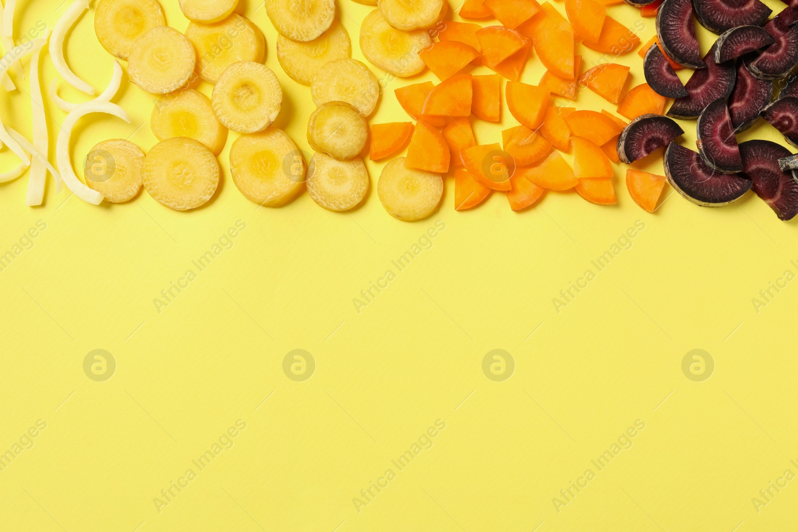 Photo of Pieces of raw color carrots on yellow background, flat lay. Space for text