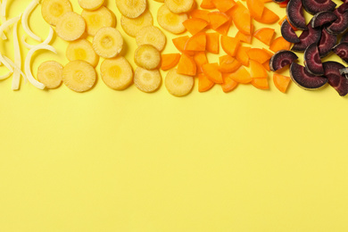 Photo of Pieces of raw color carrots on yellow background, flat lay. Space for text