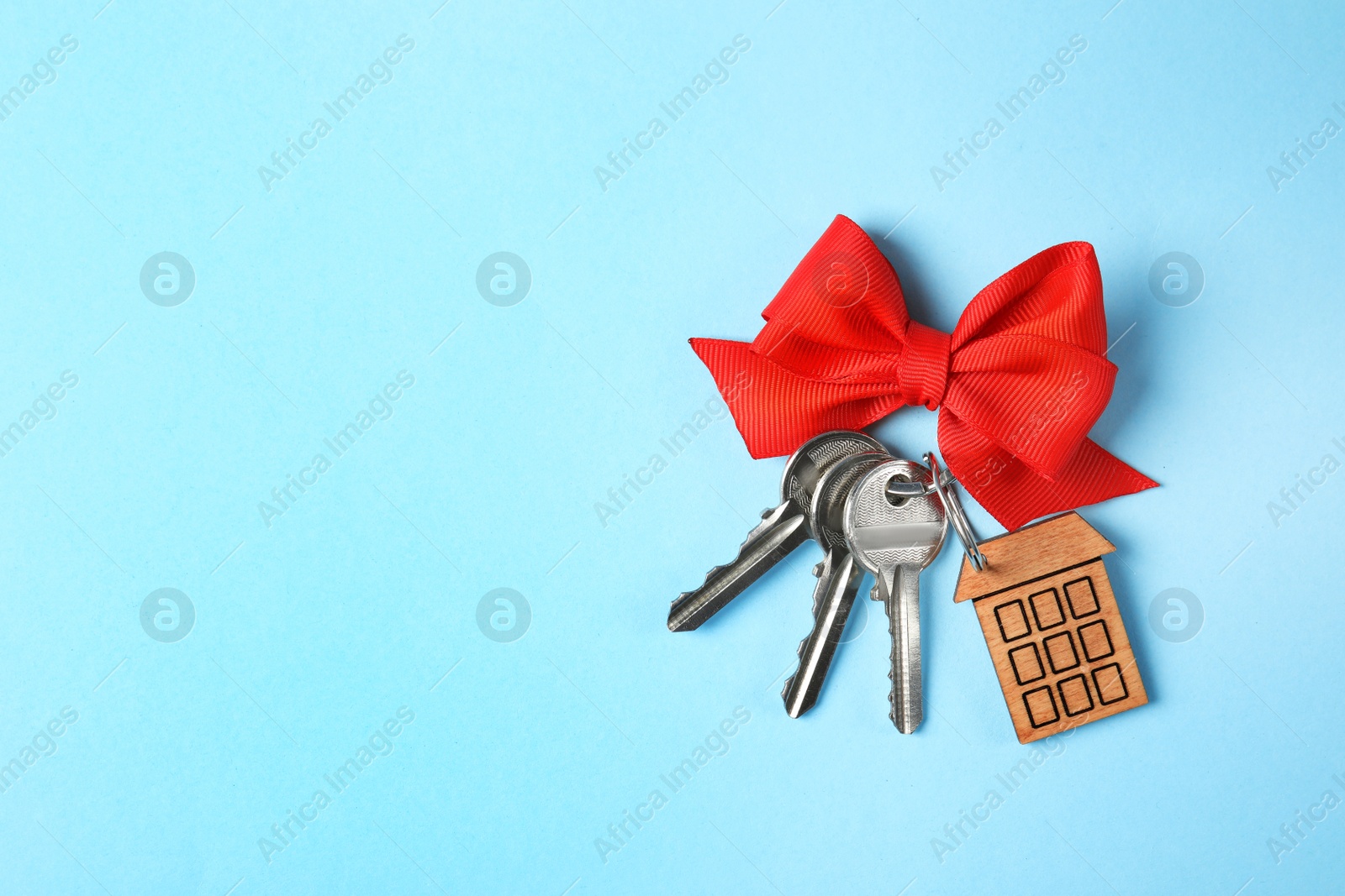 Photo of House keys with trinket and bow on color background, top view. Space for text