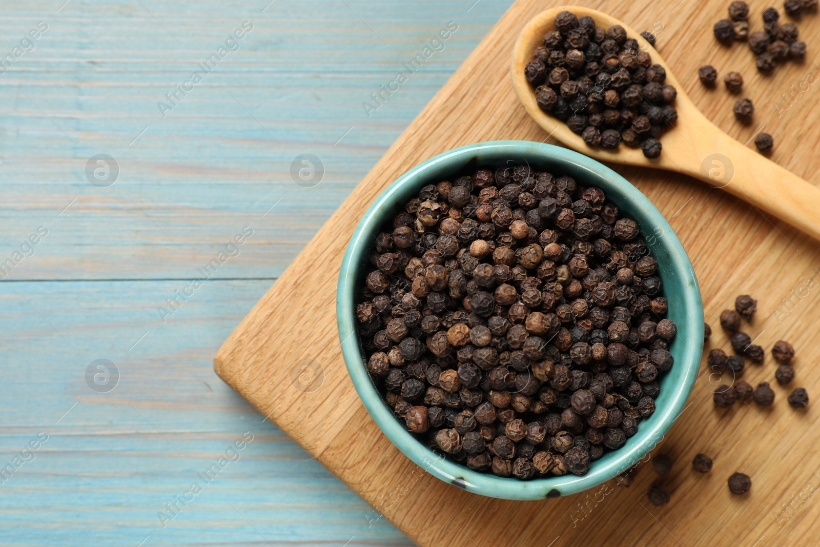 Photo of Aromatic spice. Black pepper in bowl on light blue wooden table, top view. Space for text