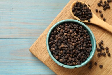 Photo of Aromatic spice. Black pepper in bowl on light blue wooden table, top view. Space for text