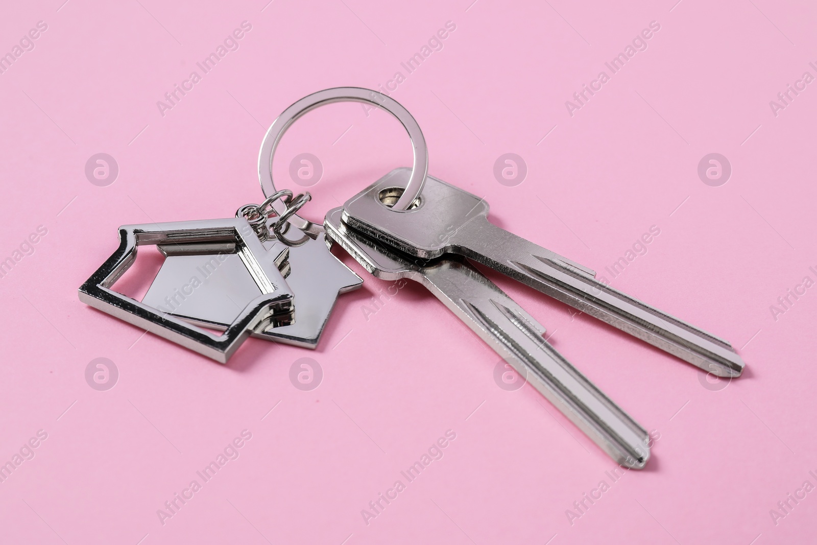 Photo of Metallic keys with keychains in shape of houses on pink background
