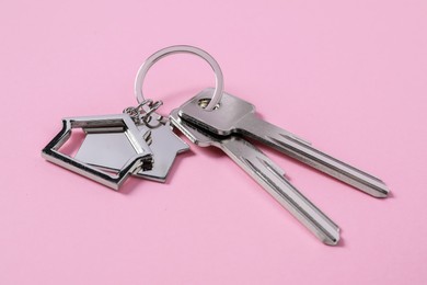 Photo of Metallic keys with keychains in shapehouses on pink background