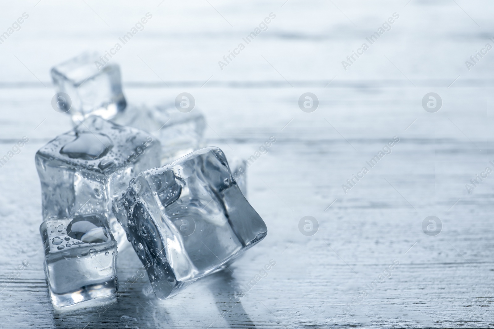 Photo of Crystal clear ice cubes with water drops on white wooden table, closeup. Space for text