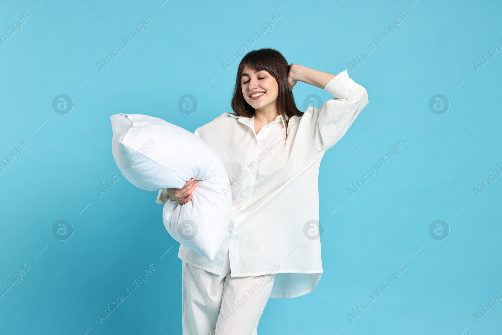 Photo of Happy woman in pyjama holding pillow on light blue background