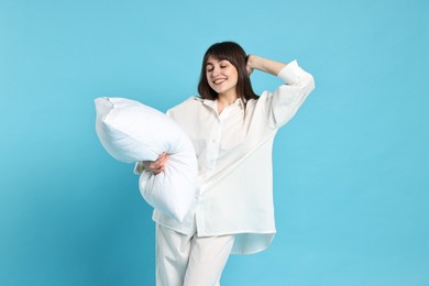 Happy woman in pyjama holding pillow on light blue background