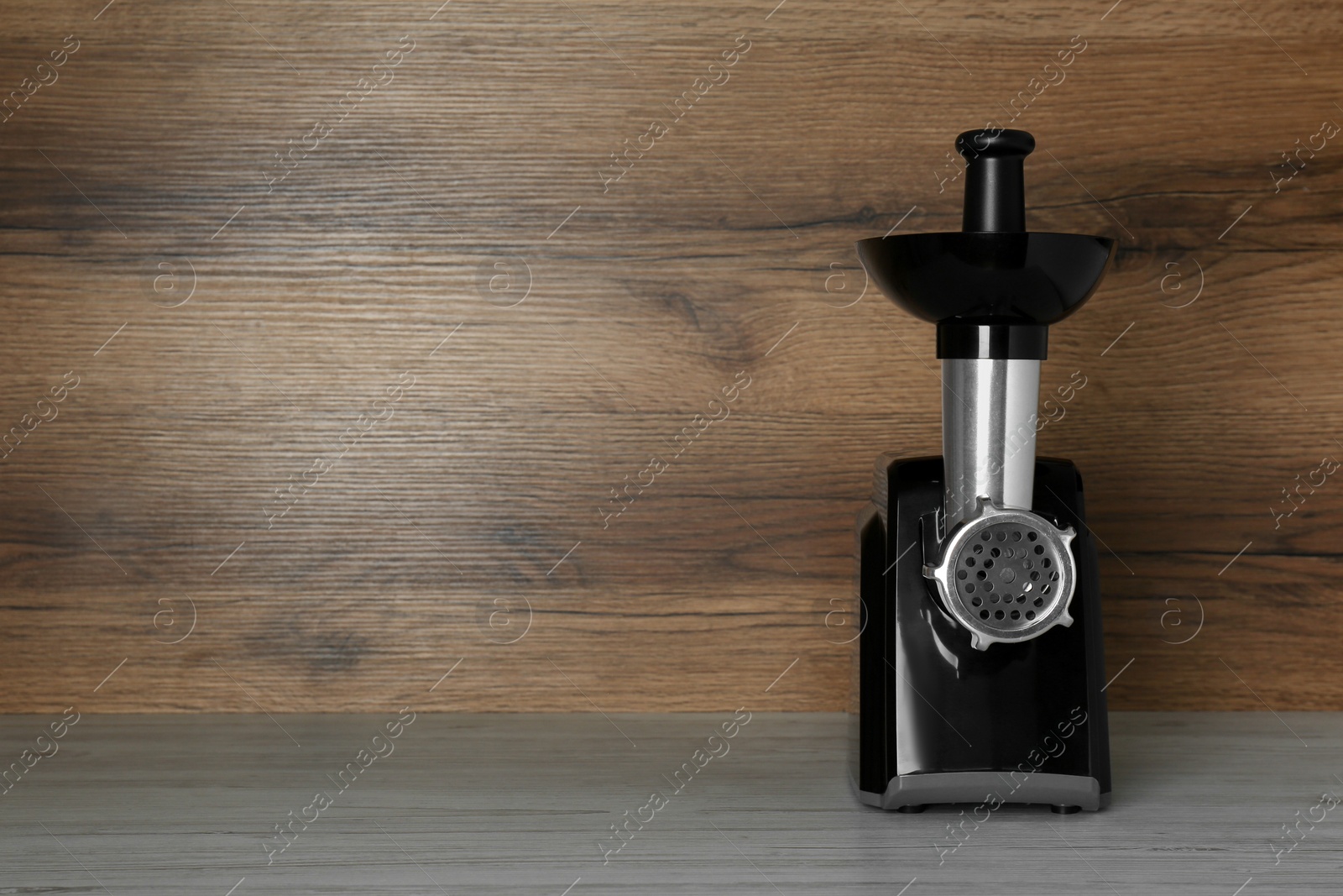 Photo of Modern electric meat grinder on light wooden table. Space for text