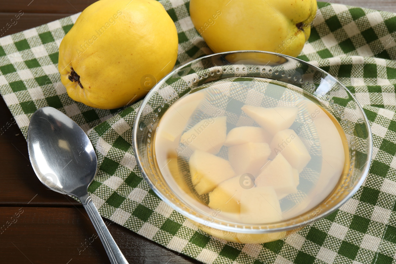 Photo of Delicious quince drink in glass bowl, fresh fruits and spoon on wooden table, closeup