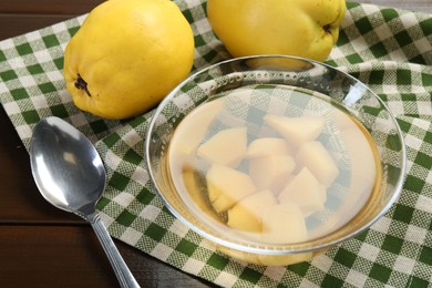 Delicious quince drink in glass bowl, fresh fruits and spoon on wooden table, closeup