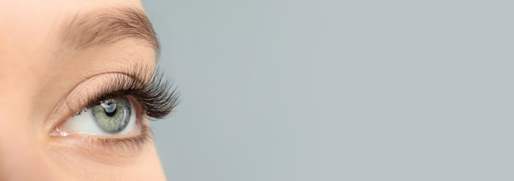 Closeup view of young woman with beautiful long eyelashes on grey background, space for text. Banner design