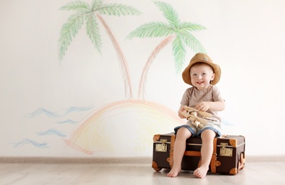 Adorable little child playing traveler with suitcase indoors