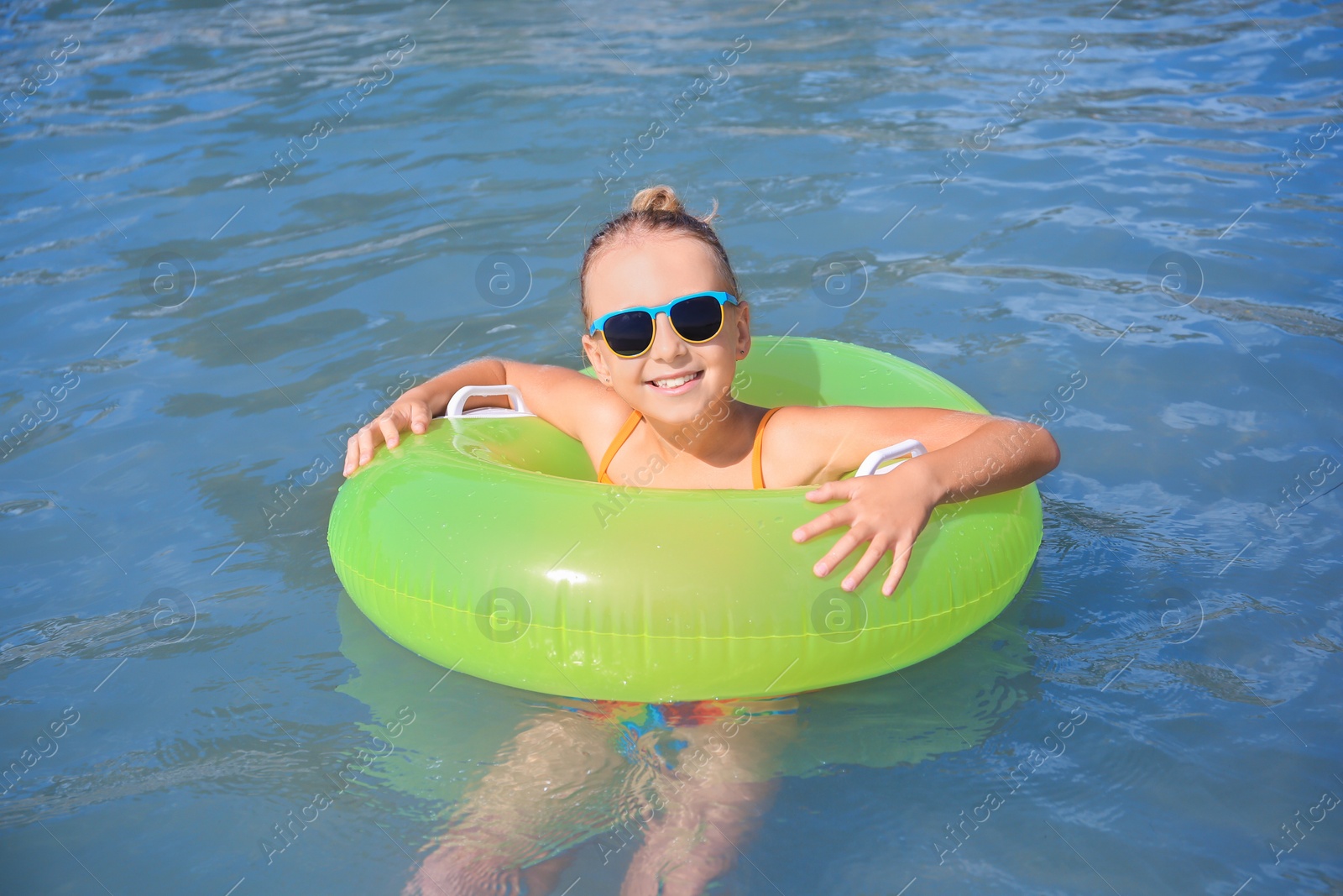 Photo of Happy little girl with sunglasses and inflatable ring in sea on sunny day. Beach holiday