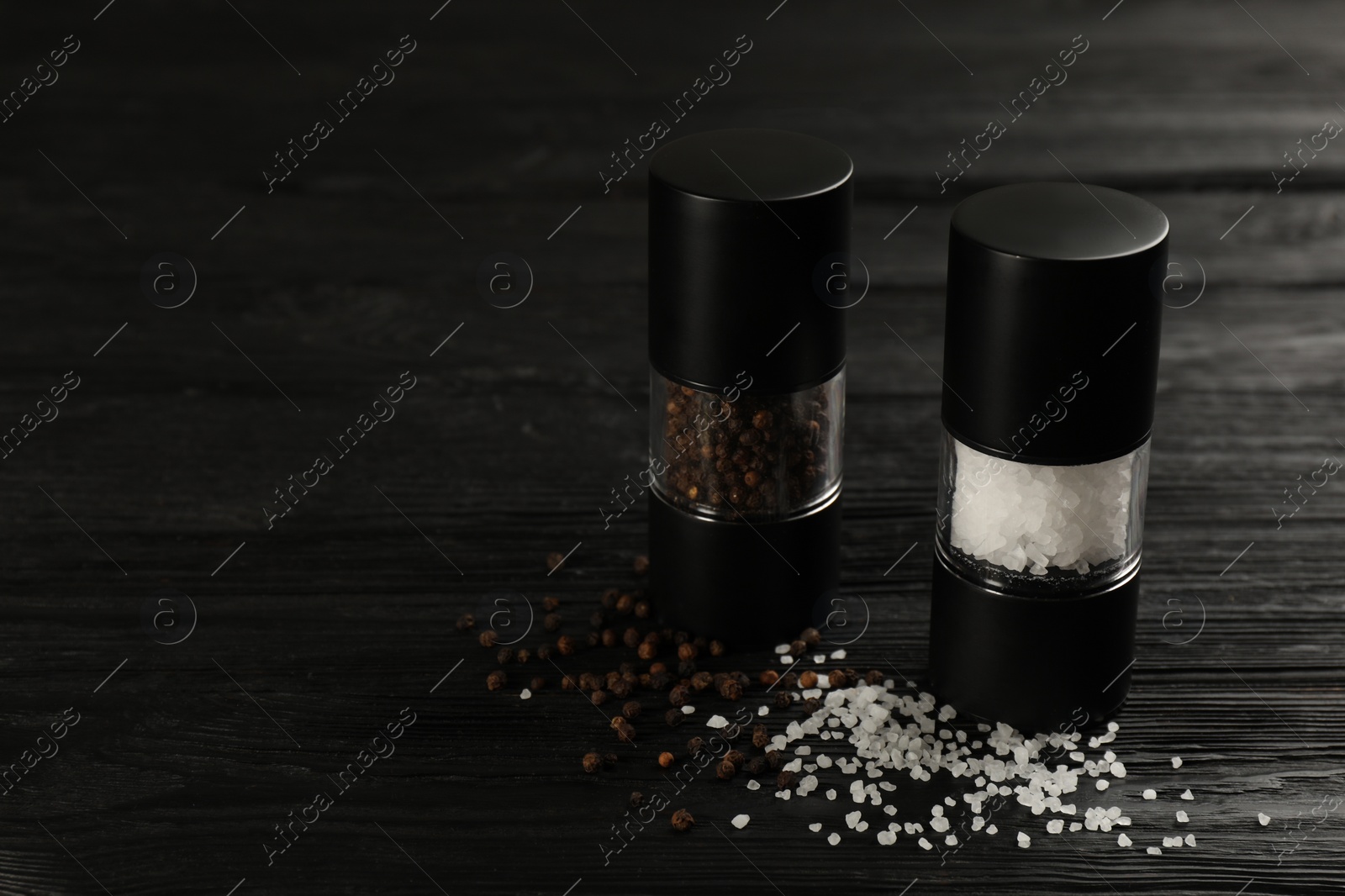 Photo of Salt and pepper shakers on black wooden table, closeup. Space for text