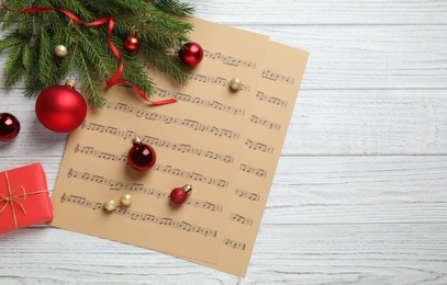 Flat lay composition with Christmas decorations and music sheets on white wooden table, space for text