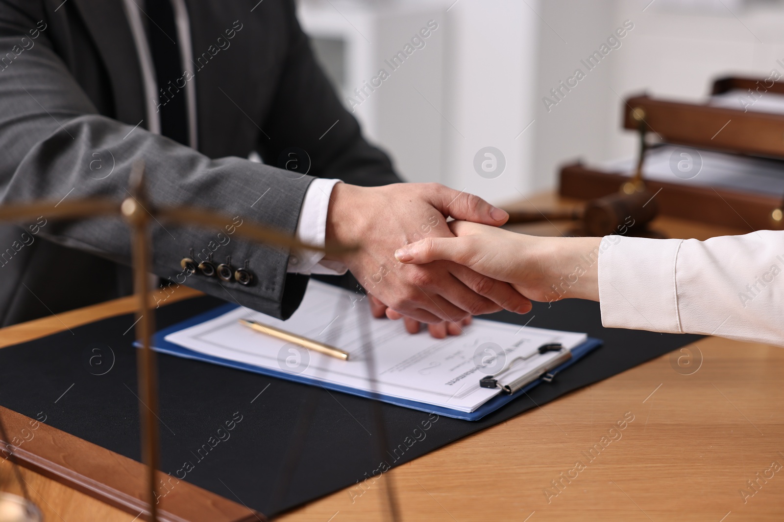 Photo of Notary shaking hands with client at wooden table in office, closeup