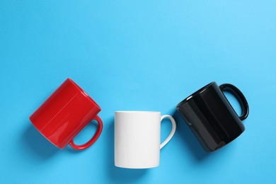 Photo of Colorful ceramic mugs on light blue background, flat lay. Space for text