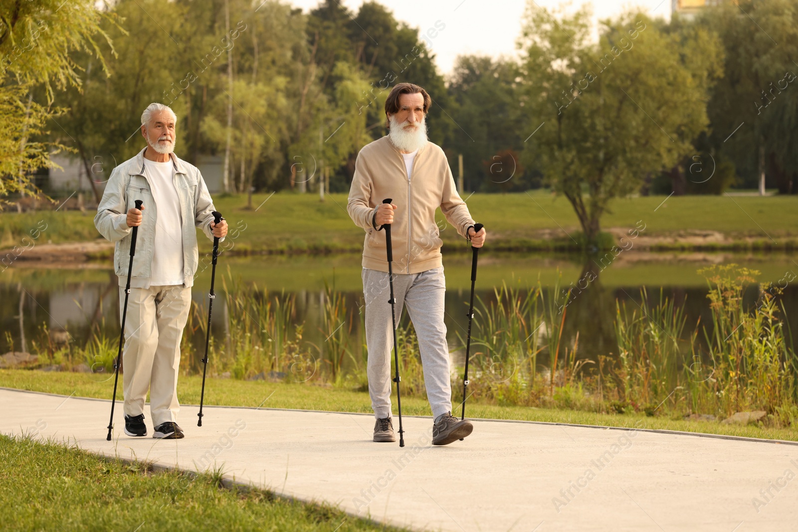 Photo of Two senior friends performing Nordic walking outdoors, space for text