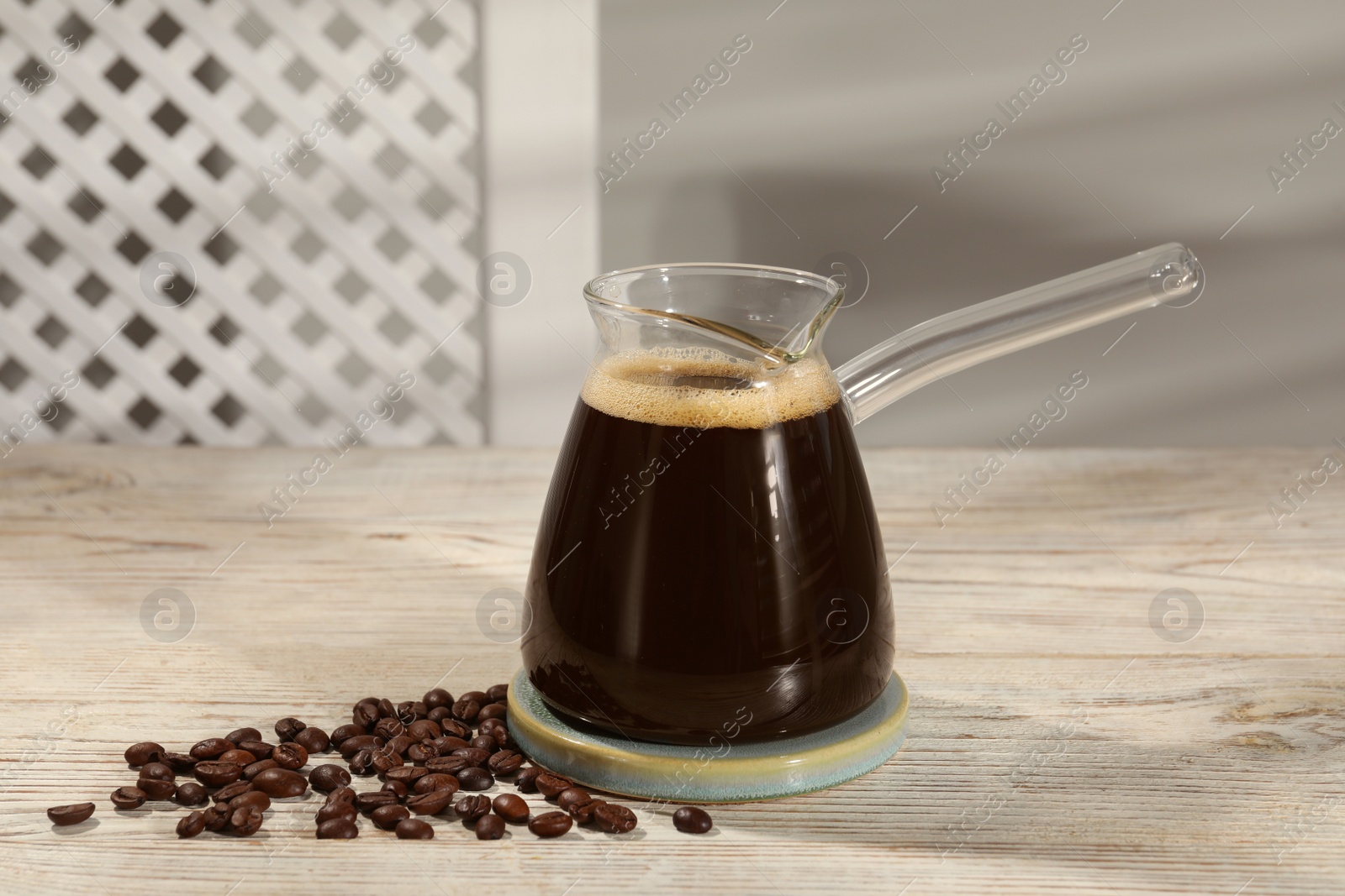 Photo of Glass turkish coffee pot with hot drink and beans on wooden table