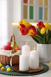 Photo of Easter decorations. Bouquet of tulips, painted eggs and burning candles on table indoors, closeup