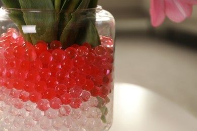 Photo of Closeup view of different color fillers in glass vase indoors, space for text. Water beads