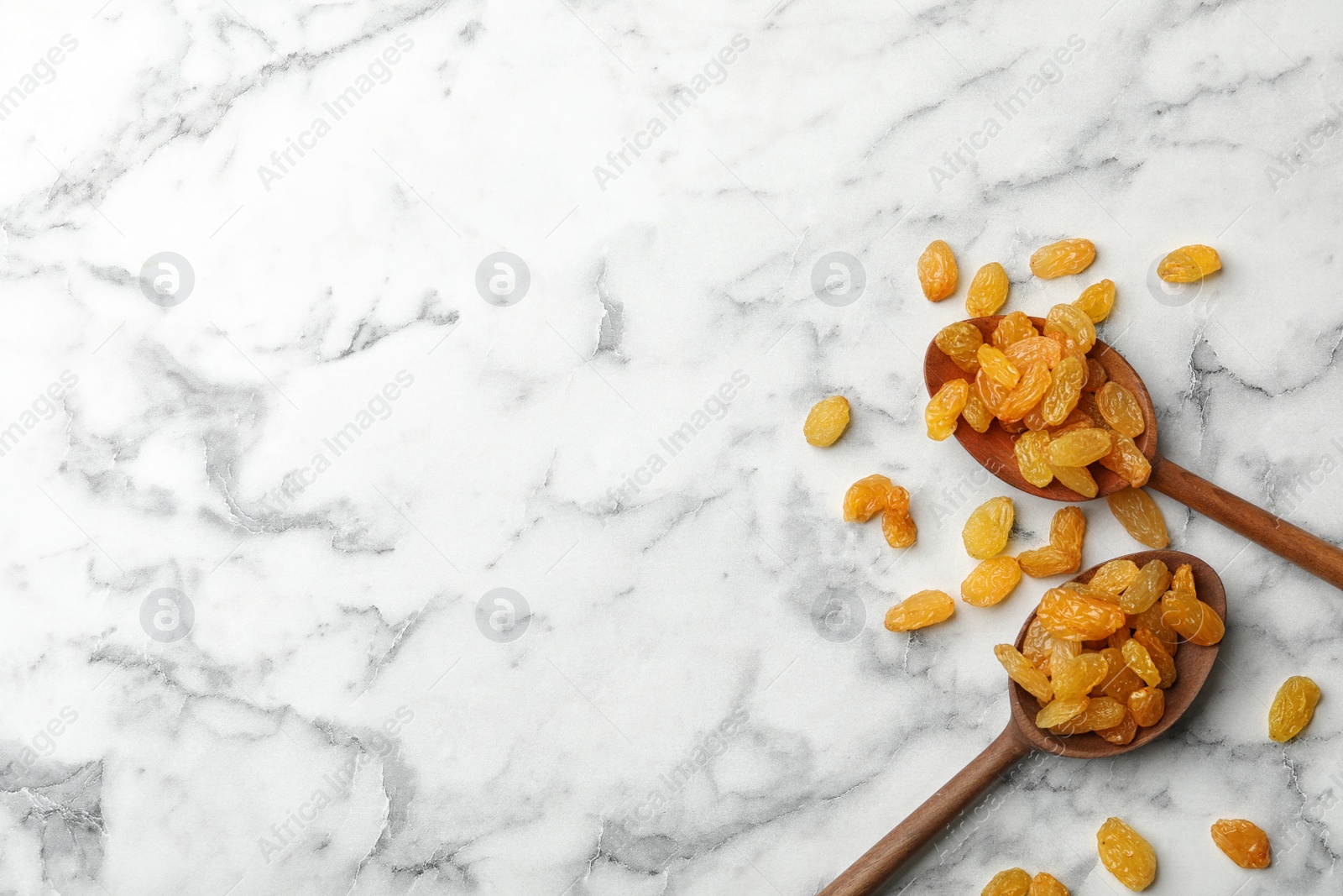 Photo of Spoons with raisins and space for text on marble background, top view. Dried fruit as healthy snack