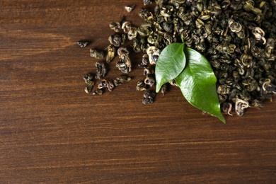 Photo of Heap of dried green tea leaves on wooden table, top view. Space for text