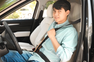 Photo of Male driver fastening safety belt in car