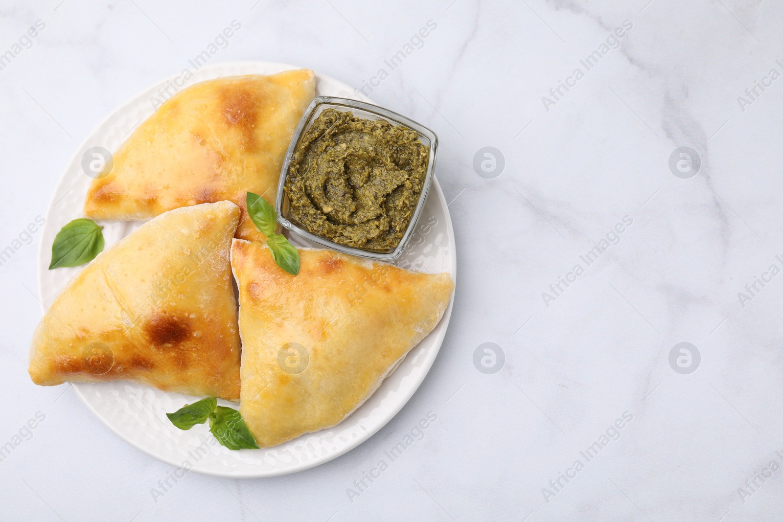 Photo of Delicious samosas with basil and pesto sauce on white marble table, top view. Space for text