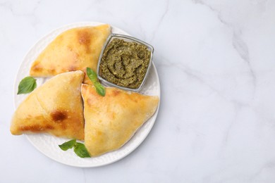 Delicious samosas with basil and pesto sauce on white marble table, top view. Space for text