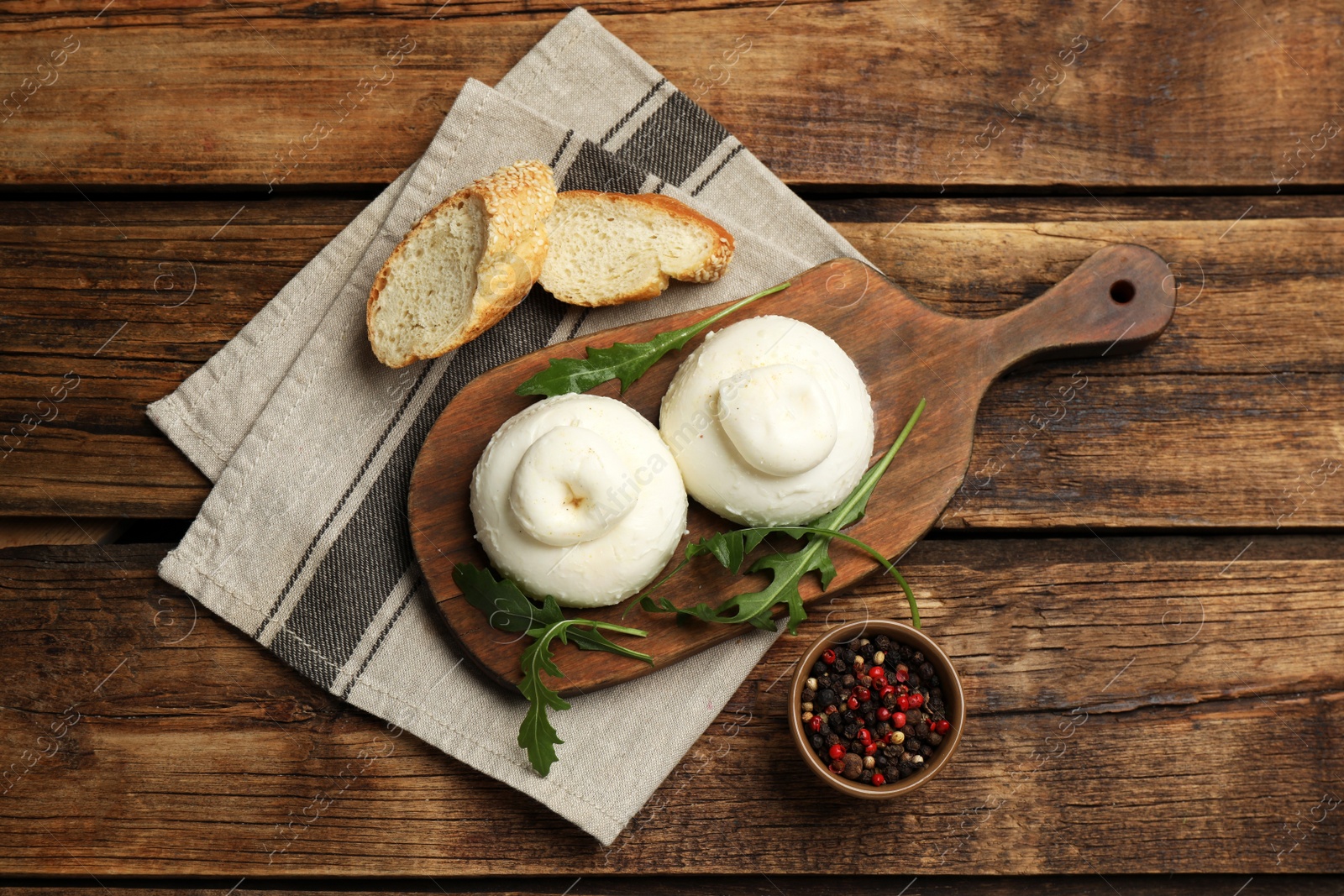 Photo of Delicious burrata cheese with arugula and fresh bread on wooden table, flat lay