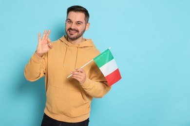 Man with flag of Italy showing ok gesture on light blue background, space for text