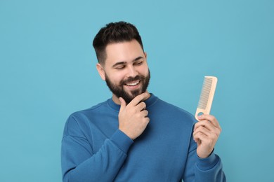 Photo of Handsome young man with mustache holding comb on light blue background