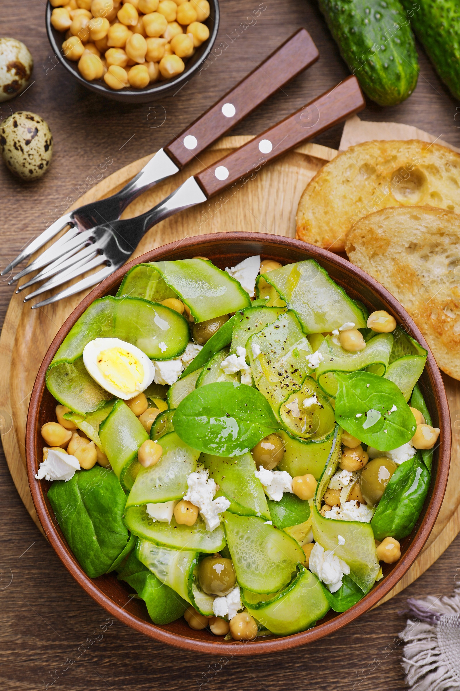 Photo of Delicious cucumber salad and toasted bread served on wooden table, flat lay